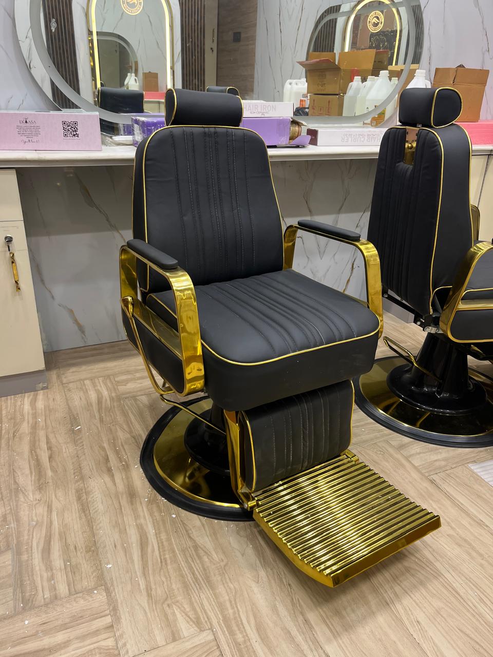 Pair of black and gold barber chairs in a marble-mirrored studio